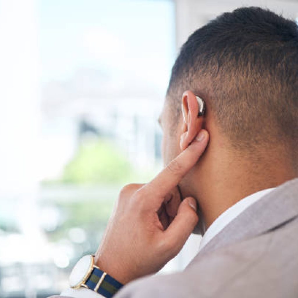 Back, business man and hearing aid for ear, sound amplifier and audio communication in company office. Professional, person with a disability and deaf with implant technology to help with listening